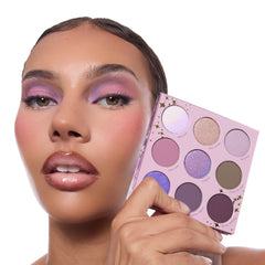 All Amethyst ColourPop Shadow Palette held beside a model’s lilac smokey eye, showing a 9‑pan lavender compact with gold star accents and matte-to-shimmer shades from soft pink and lavender to deep plum.