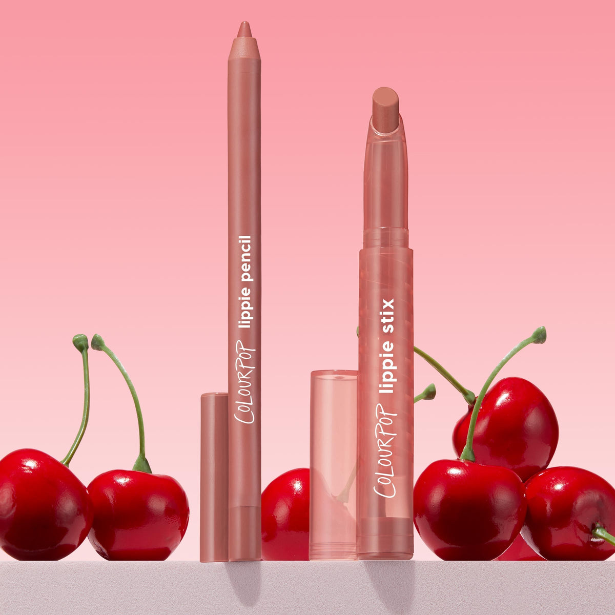 ColourPop Perfect Duo Lippie Stix + Pencil Set standing upright, revealing rosy nude tips with clear caps, framed by glossy red cherries on a pink gradient backdrop, ideal for precise lining and creamy lip color.