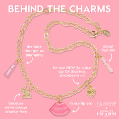 Gold chain charm necklace showcases pink enamel lips reading ColourPop, a bunny, a gold strawberry, and mini So Juicy lip oil tube charms, styled on a bubblegum-pink background for the Charmed and Juicy ColourPop So Juicy Lip Oil and Necklace Set.