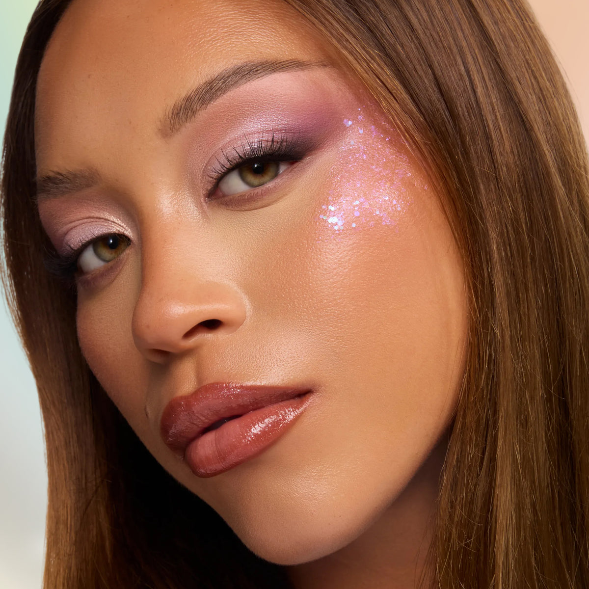 Model with medium skin wearing soft lilac shadow and Sylveon pink glitter on the cheek