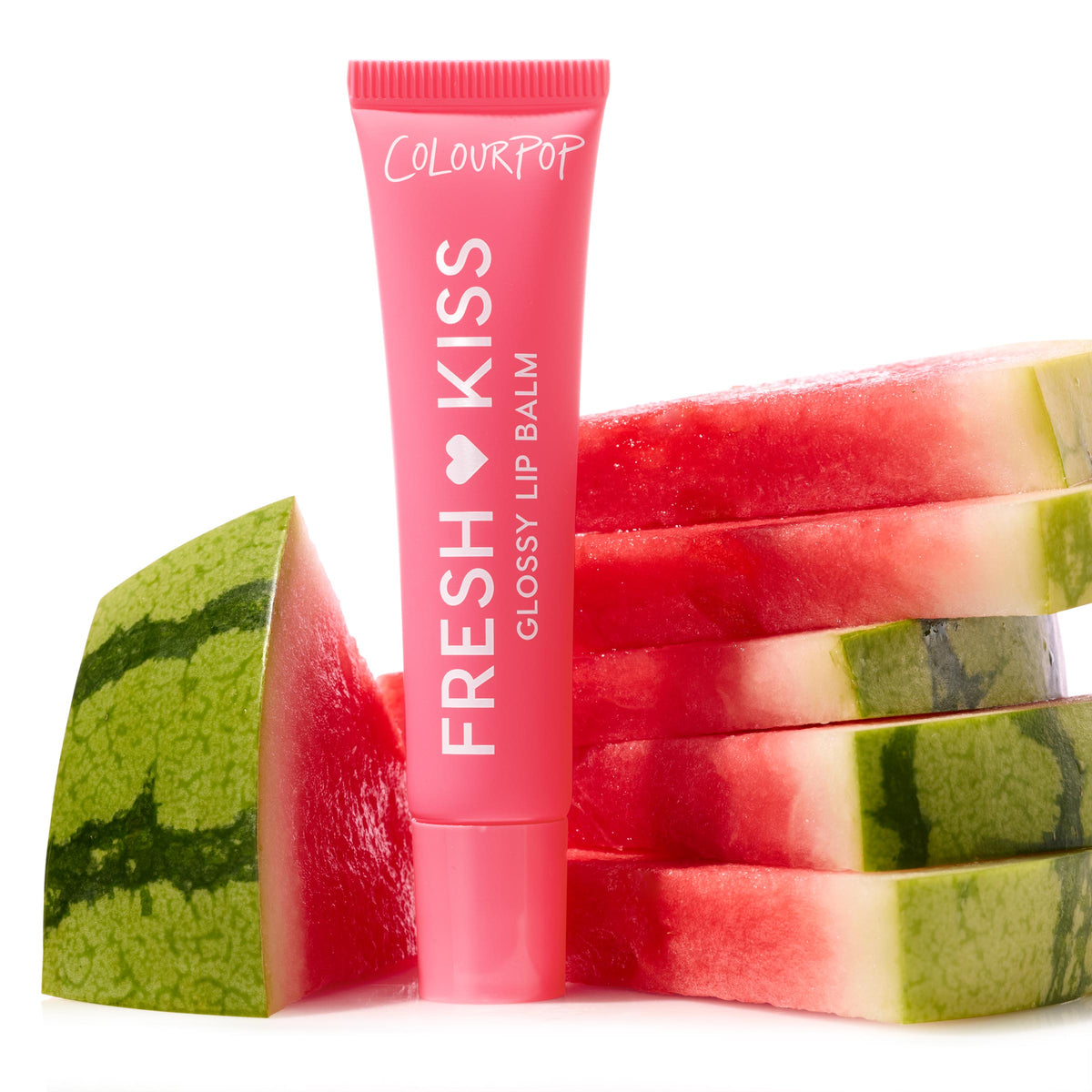Pink ColourPop Fresh Kiss glossy lip balm stands upright, framed by stacked watermelon slices on a white backdrop, spotlighting the Fruit Basket Glossy Lip Balm Trio; ideal for ColourPop Glossy Lip Balm Trio shoppers seeking juicy shine.