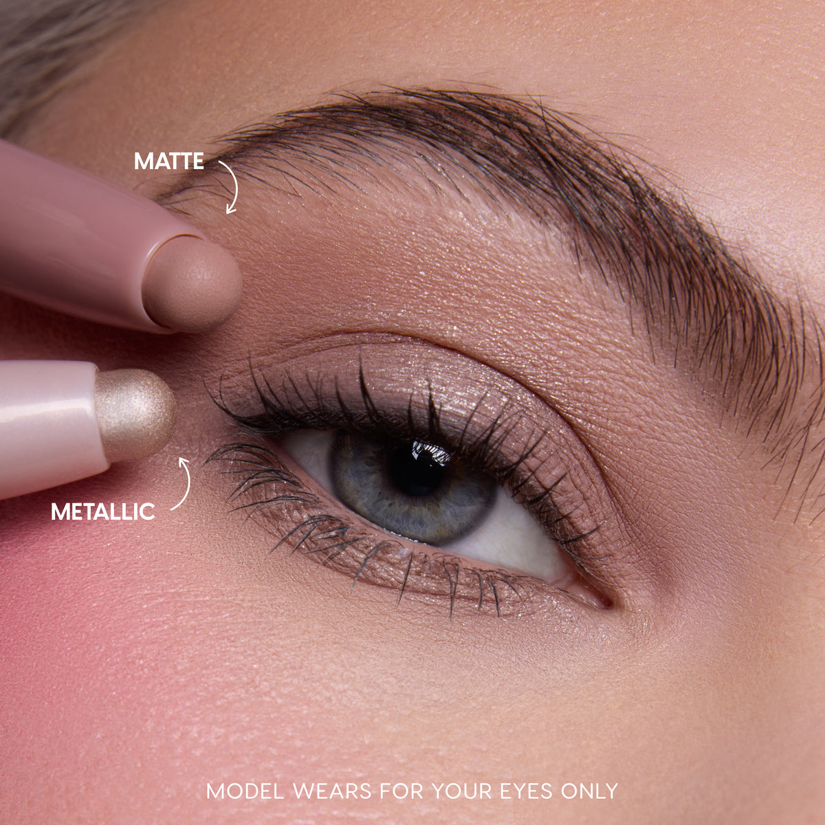 Close-up of a fair-skinned modelβs blue eye wearing shimmery neutral shadow created with the All Eyes On Me Heart to Get Shadow Stix Set, showing matte and metallic cream eyeshadow tips applying blendable color on the eyelid.
