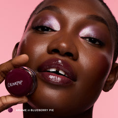Model with deep skin holding the pot, wearing Blueberry Pie Jelly Glow on her lips