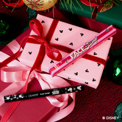 Merry Mickey Face Stamp resting on a pink gift box tied with ribbon among holiday ornaments