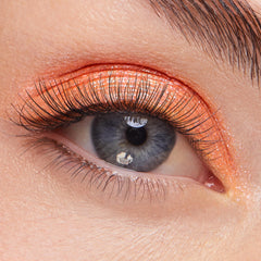Shimmery metallic orange eyeshadow with fine gold sparkle sweeps across the upper lid, showcasing ColourPop Super Shock Shadow Flamethrower on a close-up eye with long lashes for a fiery, high-shine finish.