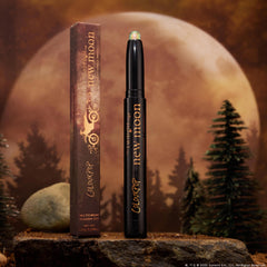 ColourPop Shadow Stix 'It’s Always Been Him' stands uncapped, revealing a shimmery green multichrome tip on a black twist-up stick with gold lettering, beside its box on a rock, framed by pine trees and a glowing full moon.