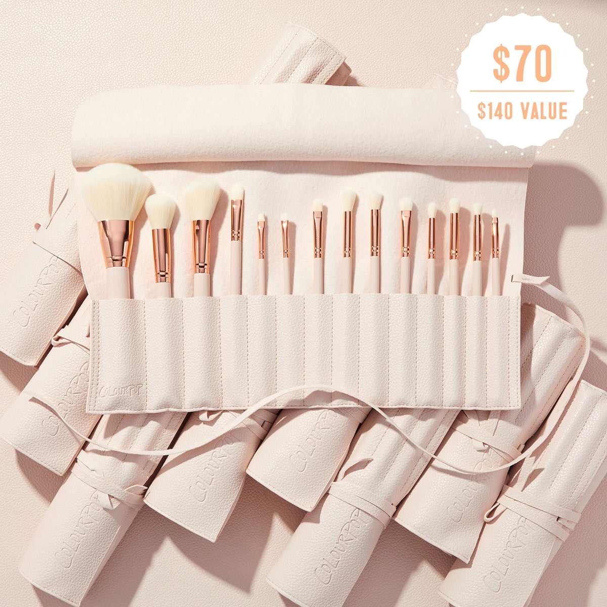 ColourPop Doin’ the Most brushes fanned in a soft pink travel roll, rose‑gold ferrules and white bristles on display, promoting the ColourPop Shadow Palette & Brush Set with $70 ($140 value) badge against a blush textured background.