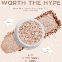 ColourPop Ritz Super Shock Shadow single, a metallic champagne‑taupe eyeshadow with silvery sparkle, shown in an open white pot with honeycomb texture as crushed pigment swipes across a nude backdrop with star graphics and hype callouts.