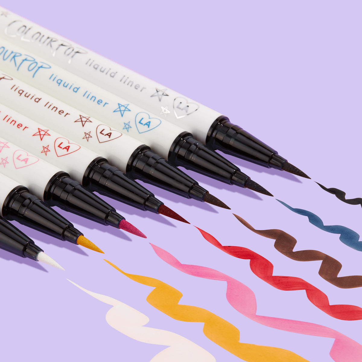 ColourPop Graceland BFF Liquid Liner creates a bold white squiggle beside multicolor swatches, the felt‑tip pen and doodled white barrel angled on a lavender background, showcasing precise application and opaque, quick‑dry wear.