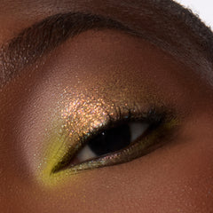 Close-up of a deep-skin eye wearing golden bronze shimmer with a lime green lower lash line from the Eeveelution palette