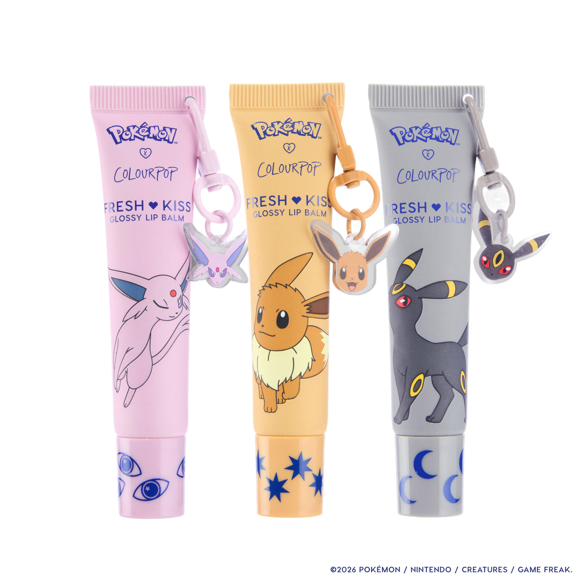 Espeon lilac, Eevee tan and Umbreon grey Fresh Kiss Glossy Lip Balm tubes, each with its Pokémon keychain charm
