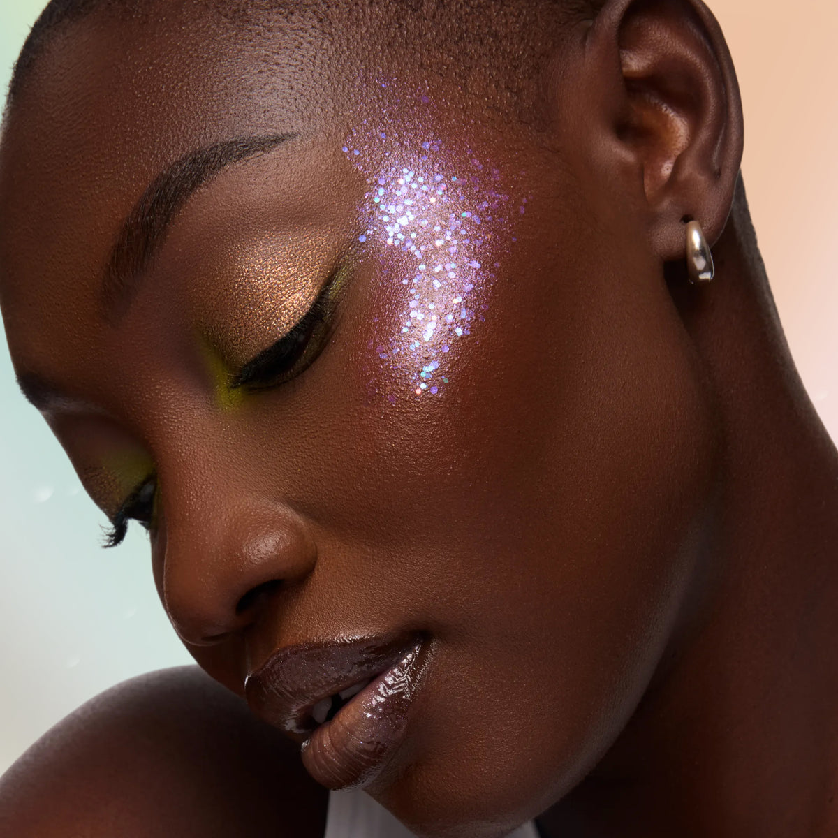 Model with deep skin wearing Sylveon pink glitter on her cheekbone with golden bronze shadow