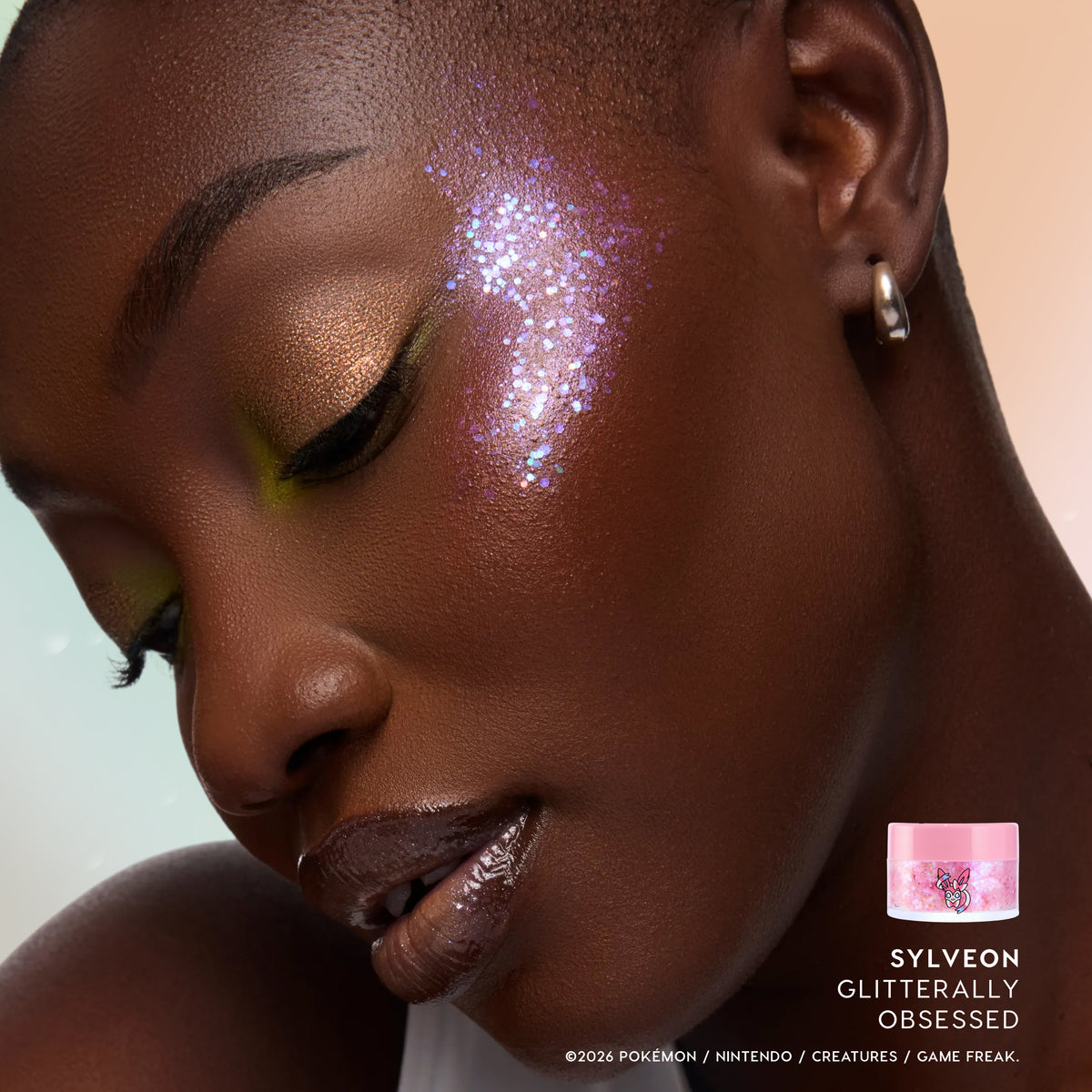 Model with deep skin wearing Sylveon Glitterally Obsessed glitter on her cheekbone with golden bronze shadow