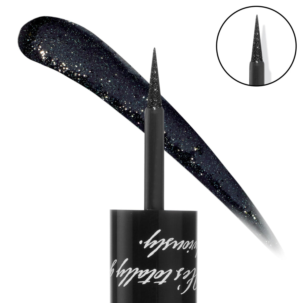 ColourPop Coven Graphix Ink Liner draws a sharp wing with an ultra-fine brush tip, shown beside a sweeping swatch of deep midnight black packed with silver sparkle; macro of the tip and glossy black cap with script on a white background.