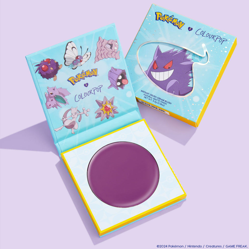 Hypnosis ColourPop Cream Blush compact opens to reveal a rich plum-purple pan, set in a yellow-and-blue Pokémon collab palette; Gengar art on the box and other Pokémon on the lid, resting on a pastel lavender surface.
