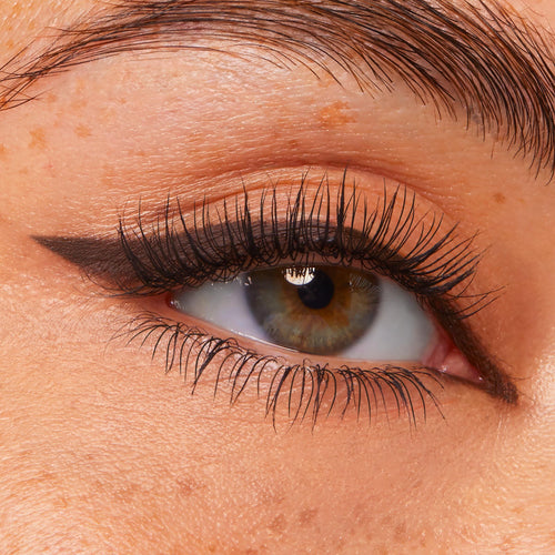 Eye wearing ColourPop Crème Gel Liner in Brew Haha, drawing a sharp coffee-brown cat-eye wing along the upper lash line, with lifted lashes and natural skin texture in close-up.