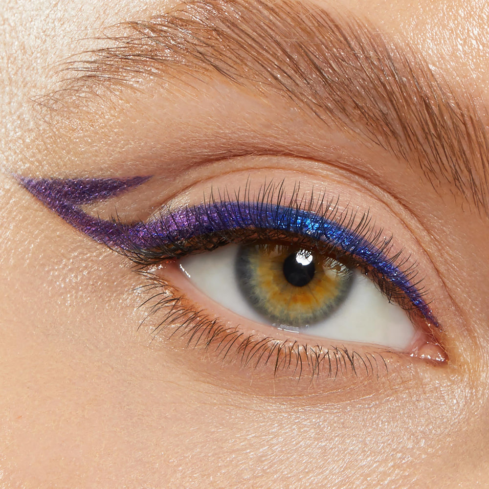 Shifting blue-to-violet winged liner defines the upper lash line and extends into a sharp double wing, showcasing Ventura Blvd, a ColourPop Chrome Crème Gel Liner, on a close-up eye with soft natural lashes and brow.