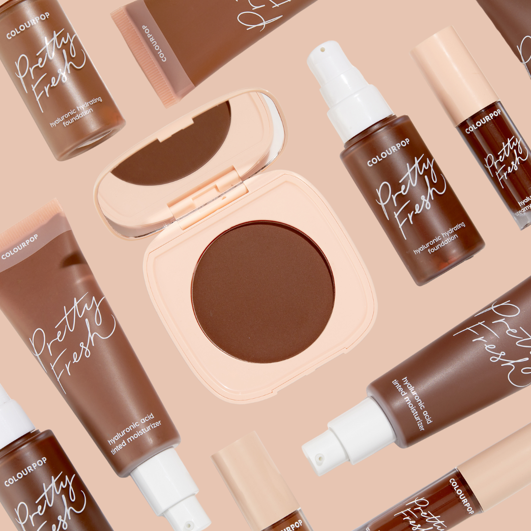 ColourPop Pretty Fresh Tinted Moisturizer in Dark 20 N rests in a flat lay, surrounded by coordinating Pretty Fresh foundation bottles and a compact on a peach background, showcasing the deep, hydrating hyaluronic formula.