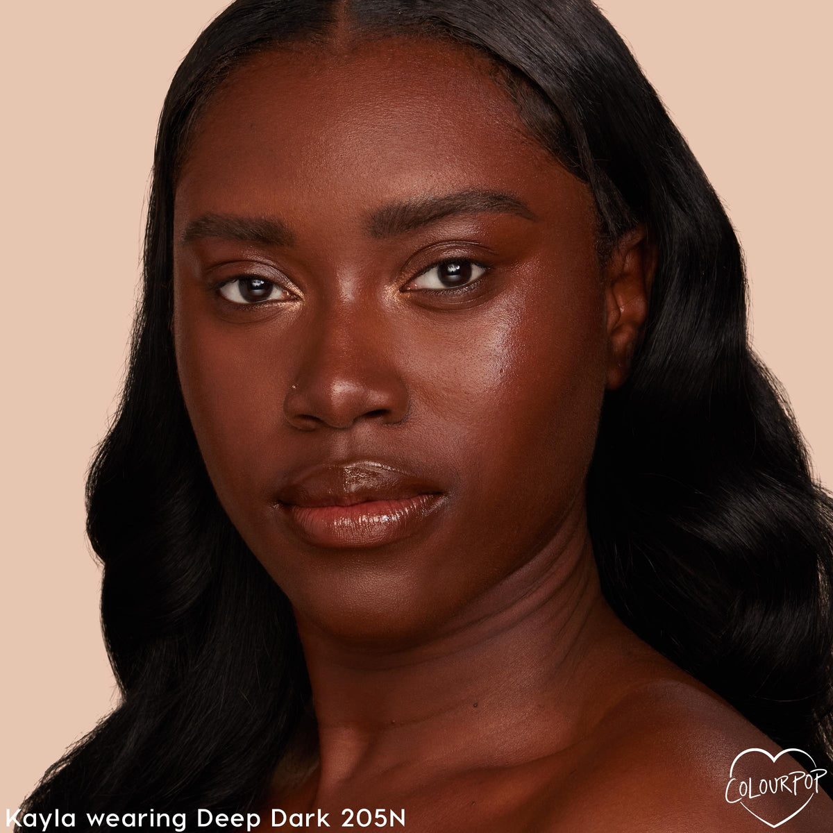 Model wearing ColourPop Pretty Fresh Creamy Concealer shade Deep Dark 205 N, showing a smooth, natural, hydrated finish that evens under‑eyes and complexion in a close‑up headshot against a soft beige background.