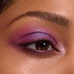 Shimmering fuchsia-to-lilac eyeshadow glows on a brown eye, blended across lid and crease with an inner-corner highlight, showcasing the Rainbow Rush ColourPop Shadow Palette Set in a studio close-up with groomed brow and soft lighting.
