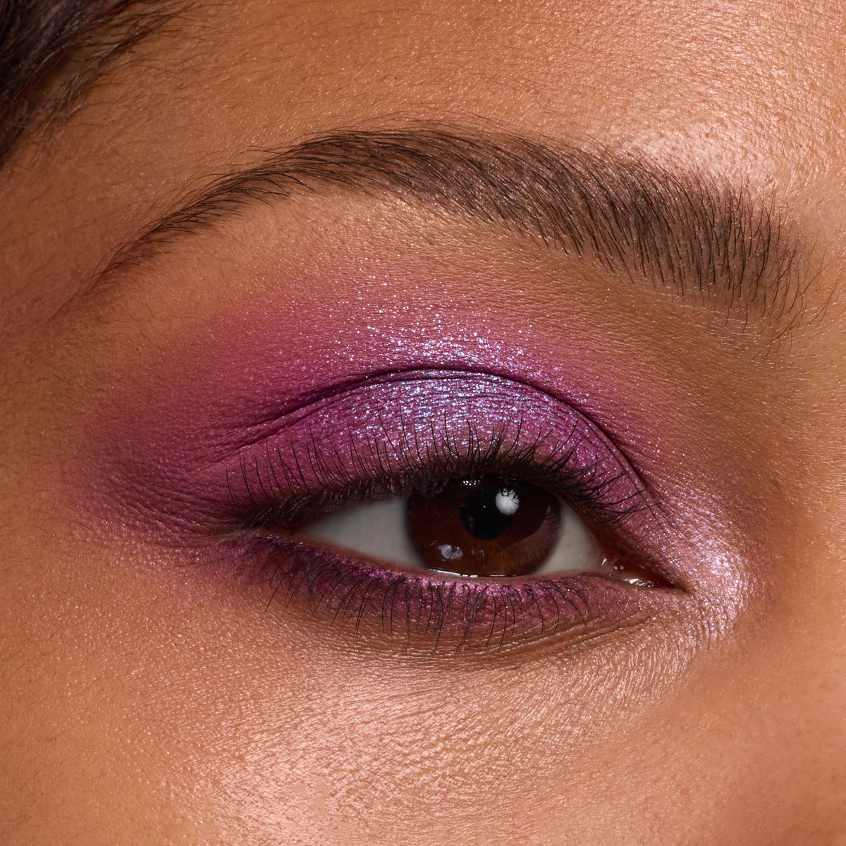 Shimmering fuchsia-to-lilac eyeshadow glows on a brown eye, blended across lid and crease with an inner-corner highlight, showcasing the Rainbow Rush ColourPop Shadow Palette Set in a studio close-up with groomed brow and soft lighting.