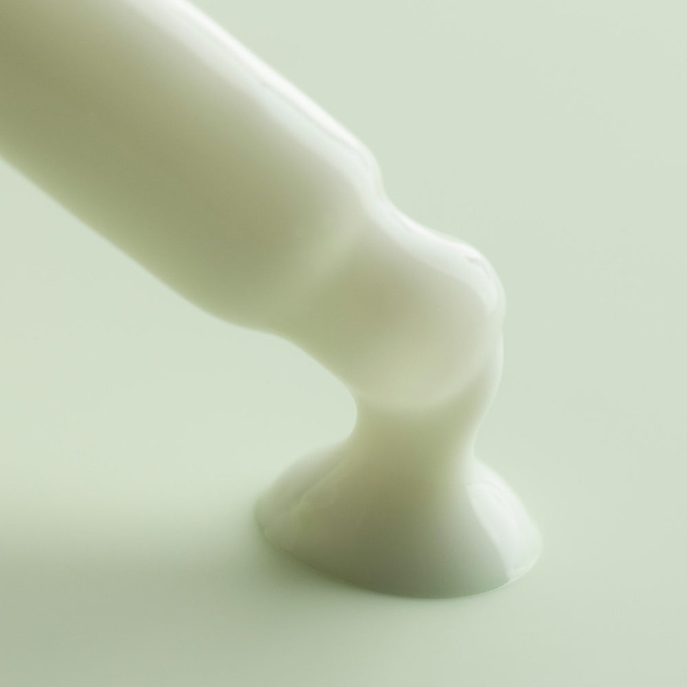 Matcha Face Milk flowing from an applicator tip and pooling into a glossy white puddle on a soft mint background, highlighting the creamy texture of ColourPop Face Milk skincare.