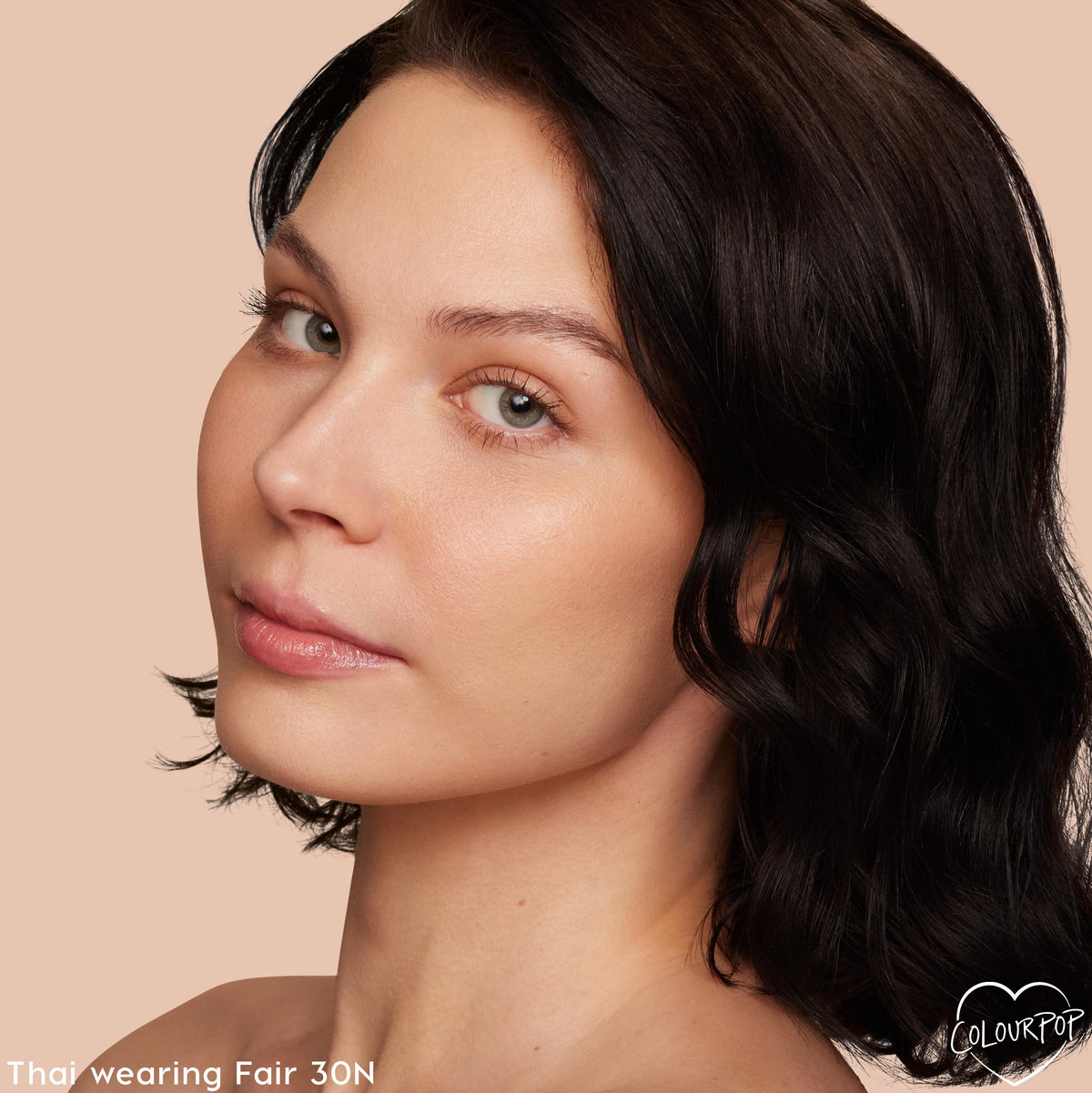 Model wearing Fair 30 N, showcasing ColourPop Hyaluronic Hydrating Foundation with a smooth, dewy, natural finish on fair neutral skin; close-up head tilt against a soft beige background with a small ColourPop heart logo in the corner.