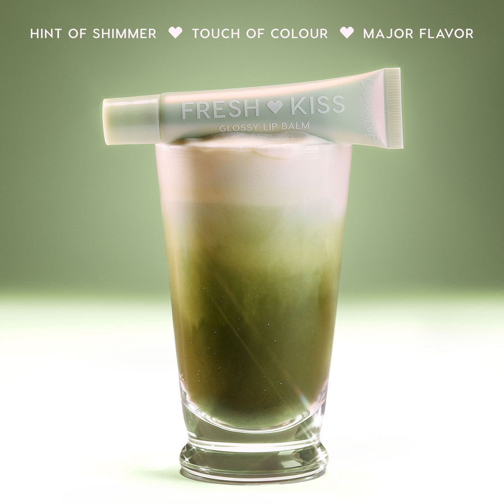 ColourPop Vanilla Matcha Fresh Kiss Glossy Balm with pearl finish rests open across a layered iced matcha latte, glossy Lip Gloss & Lip Oil texture glistening under bright studio lights against a bold pink backdrop.