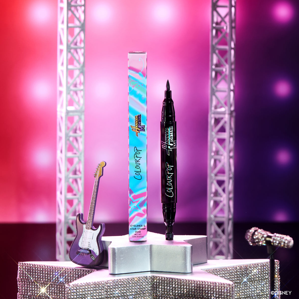 Double Life Eyeliner and Star Stamp Duo standing beside its box on a concert stage set with a guitar