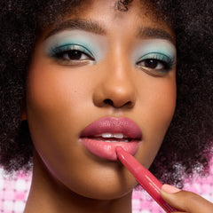 Model with deep skin wearing aqua eyeshadow, applying a pink Lippie Stix from the Hannah Montana collection