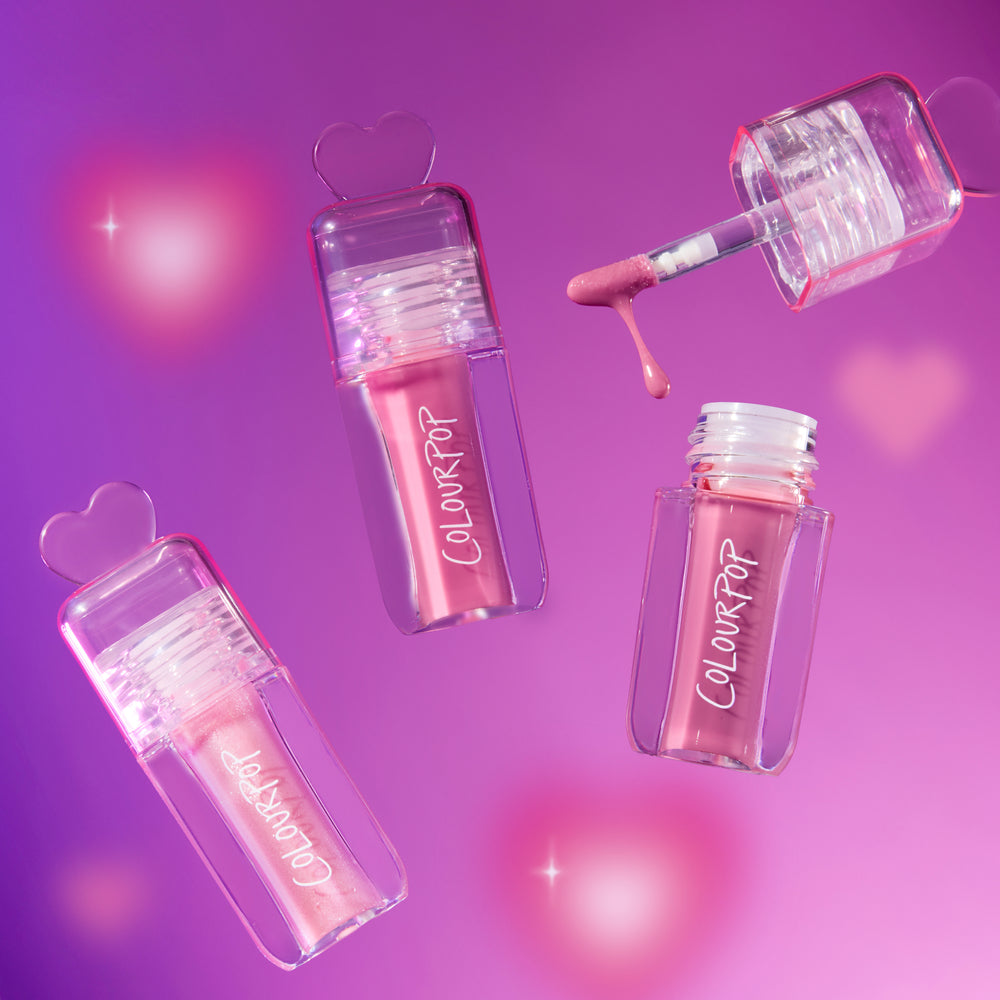 Gloss Me Up ultra glossy lip set from the Heart to Get collection, with three pink ColourPop lip gloss tubes and a dripping applicator floating on a glowing pink and purple background with heart-shaped caps.