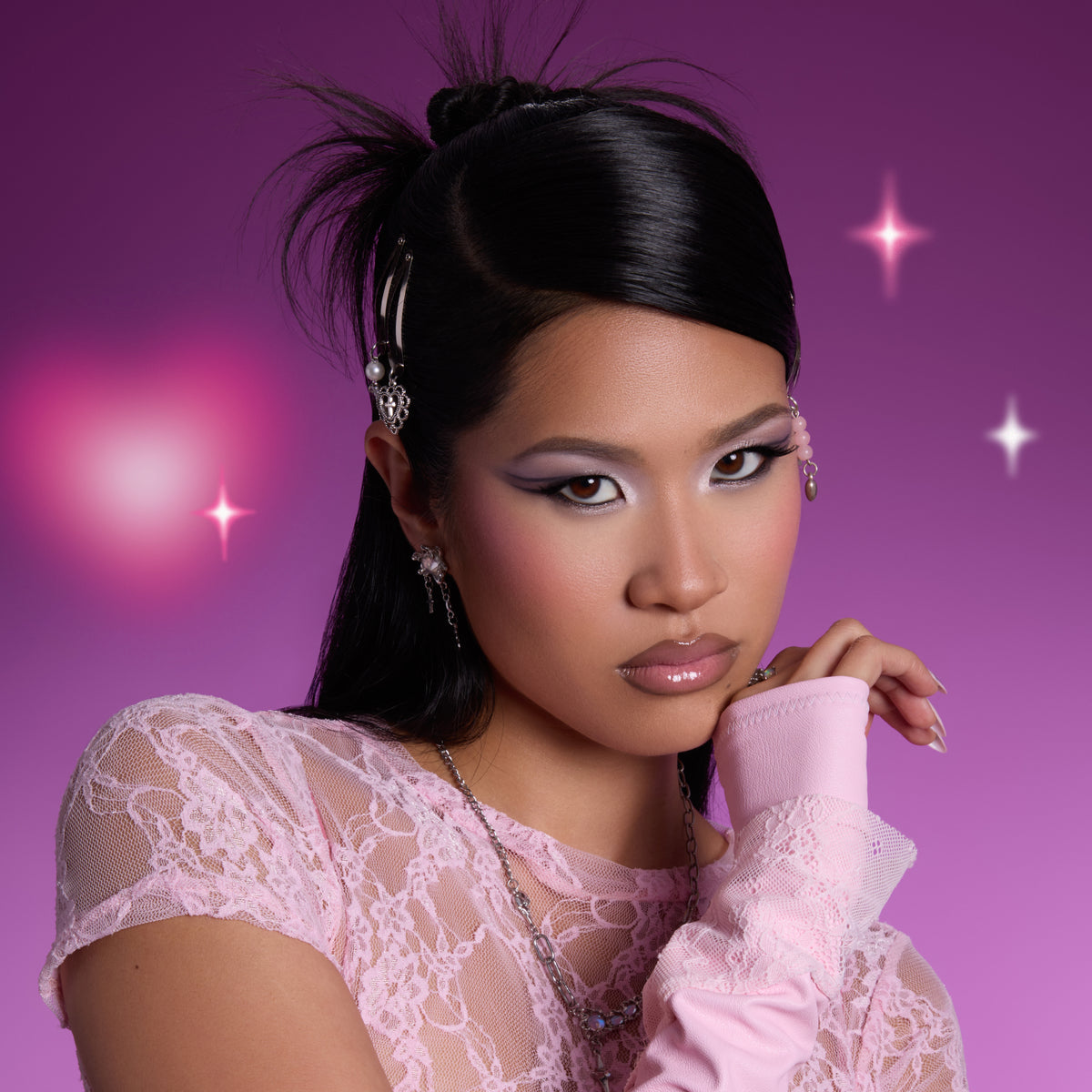 Model wearing shimmery lavender and silver eye look created with the Heart to Get shadow palette, posing against a glowing purple background with soft heart lights, showcasing bold graphic eyeshadow and glossy lips for Heart to Get makeup.