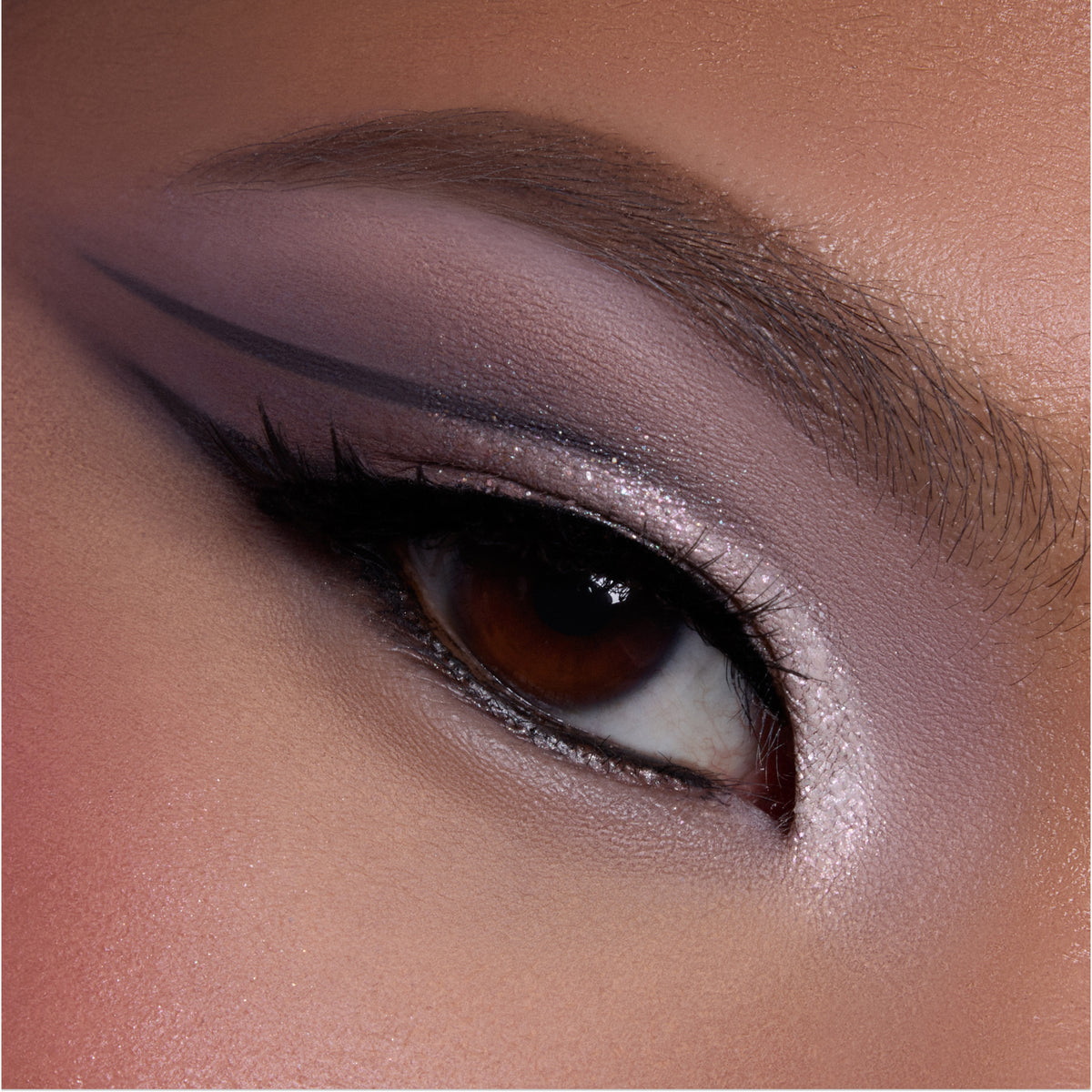 Close-up of a brown eye wearing shimmering mauve and pink shadow from the Heart to Get shadow palette, with sharp graphic black liner and highlighted inner corner, showcasing bold glam eye makeup detail.