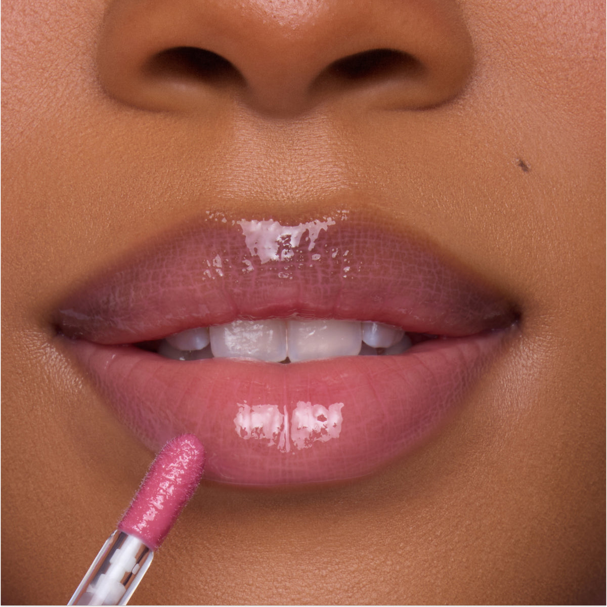 Close-up of a model applying Heart to Get Your New Obsession Ultra Glossy Lip, a high-shine pink lip gloss, with a doe-foot applicator on smooth, full lips for a juicy, plumped finish.