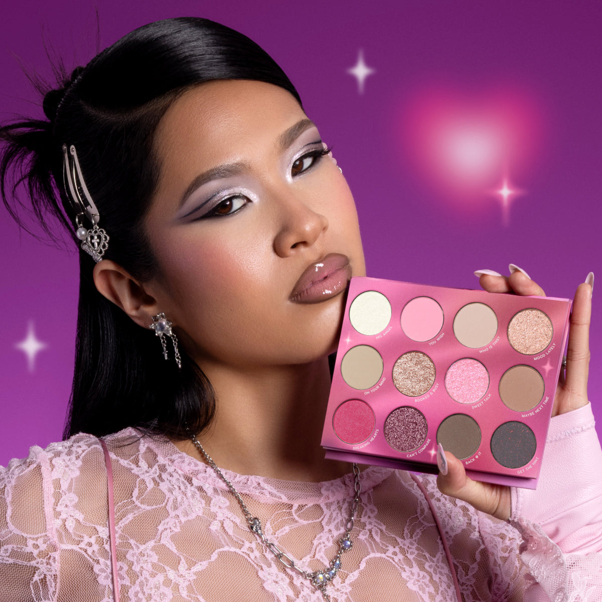 Model with bold pastel eye makeup holds the Heart to Get Full Collection eyeshadow palette, showing 12 shimmery and matte pink, nude, and berry shades against a glowing purple background, promoting the Heart to Get full collection set.