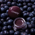 Blueberry Pie Jelly Glow Lip & Cheek Jelly, a deep berry jelly in a clear pot, on a bed of blueberries