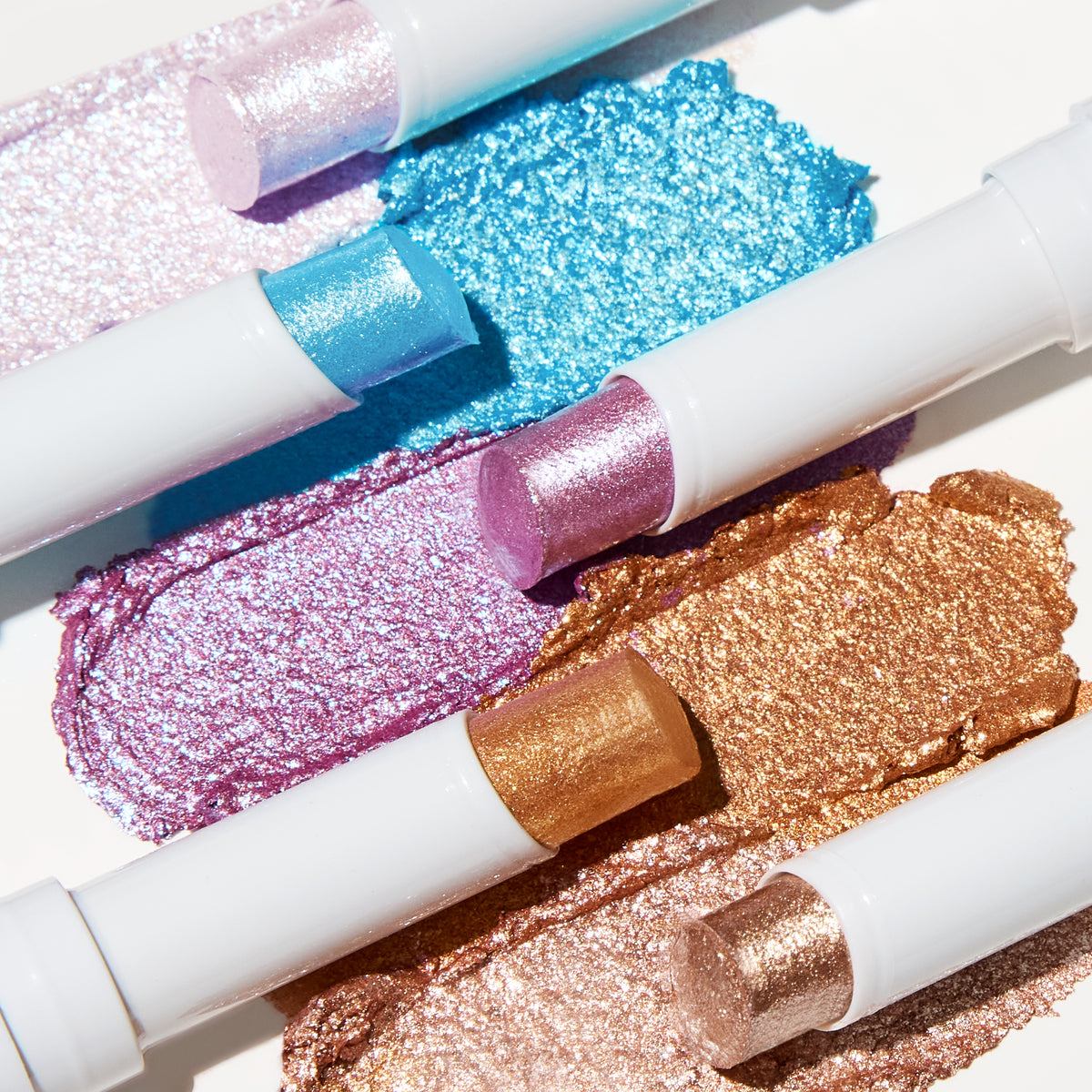 Jelly Much Gel Eyeshadow Sticks in lilac, blue and gold, uncapped over sparkly smears