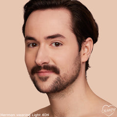 Model wearing Light 40 N, a ColourPop Hyaluronic Hydrating Foundation shade, showcases smooth, natural medium coverage with a hydrated finish; close-up face with mustache and stubble against a soft beige background.
