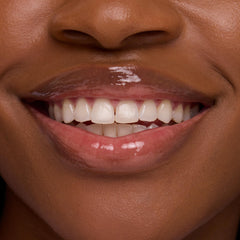 Glossy lips smile, wearing the Chocolate Milkshake ColourPop Lip Mask, delivering a clear, high-shine finish that smooths and hydrates; tight crop of mouth and teeth highlights the plush sheen for product detail.
