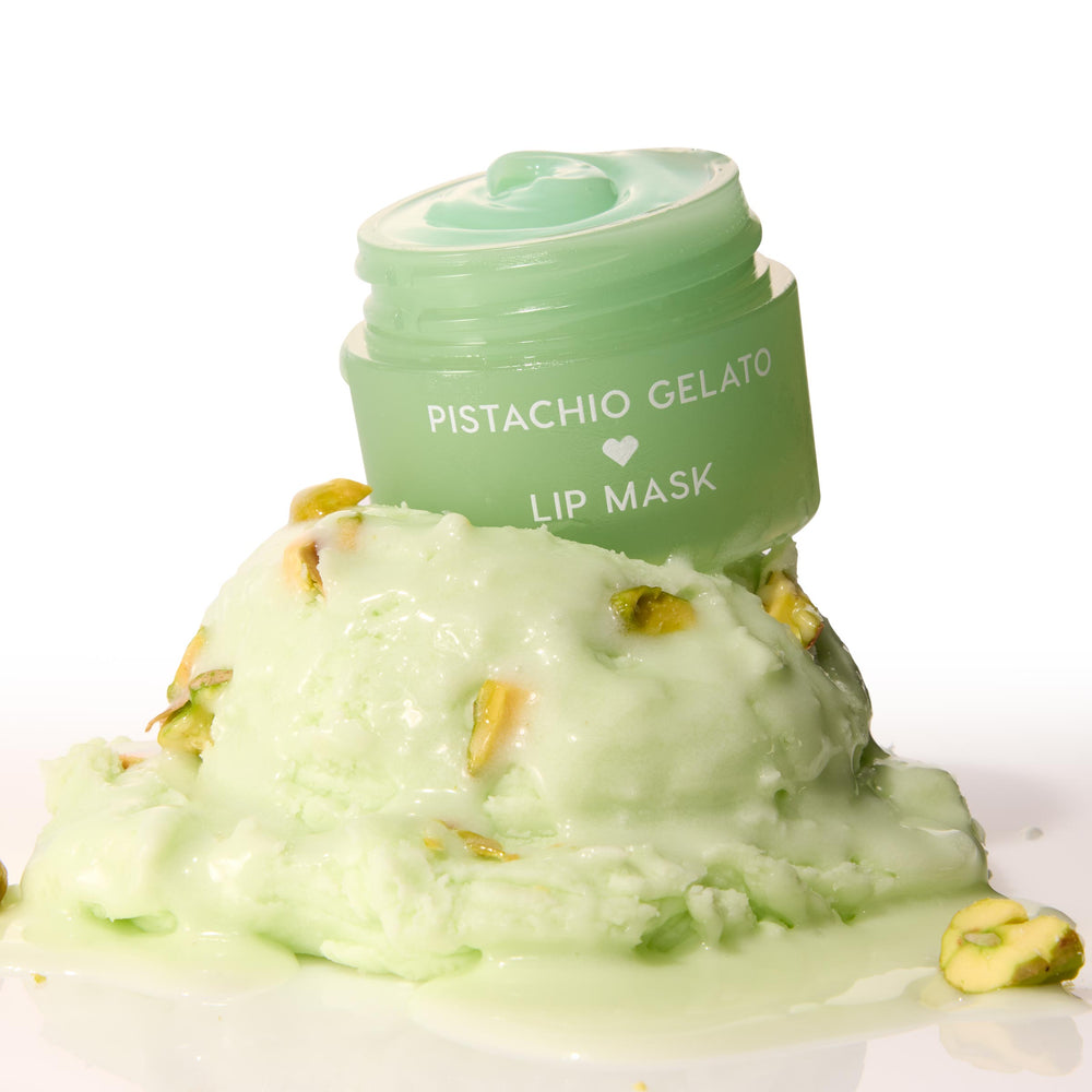 Mint-green Pistachio Gelato lip mask jar, lid off to reveal glossy balm, perched on a melting scoop of pistachio gelato with nut pieces on a white background - ColourPop Lip Mask product shot emphasizing creamy texture and dessert-inspired scent.