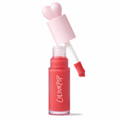 ColourPop Liquid Blush She’s Cute shown open, doe-foot applicator lifted from a frosted coral-pink bottle with a pale pink heart-shaped cap, revealing creamy formula on the tip; white backdrop with an Allure 2025 Best of Beauty award badge.