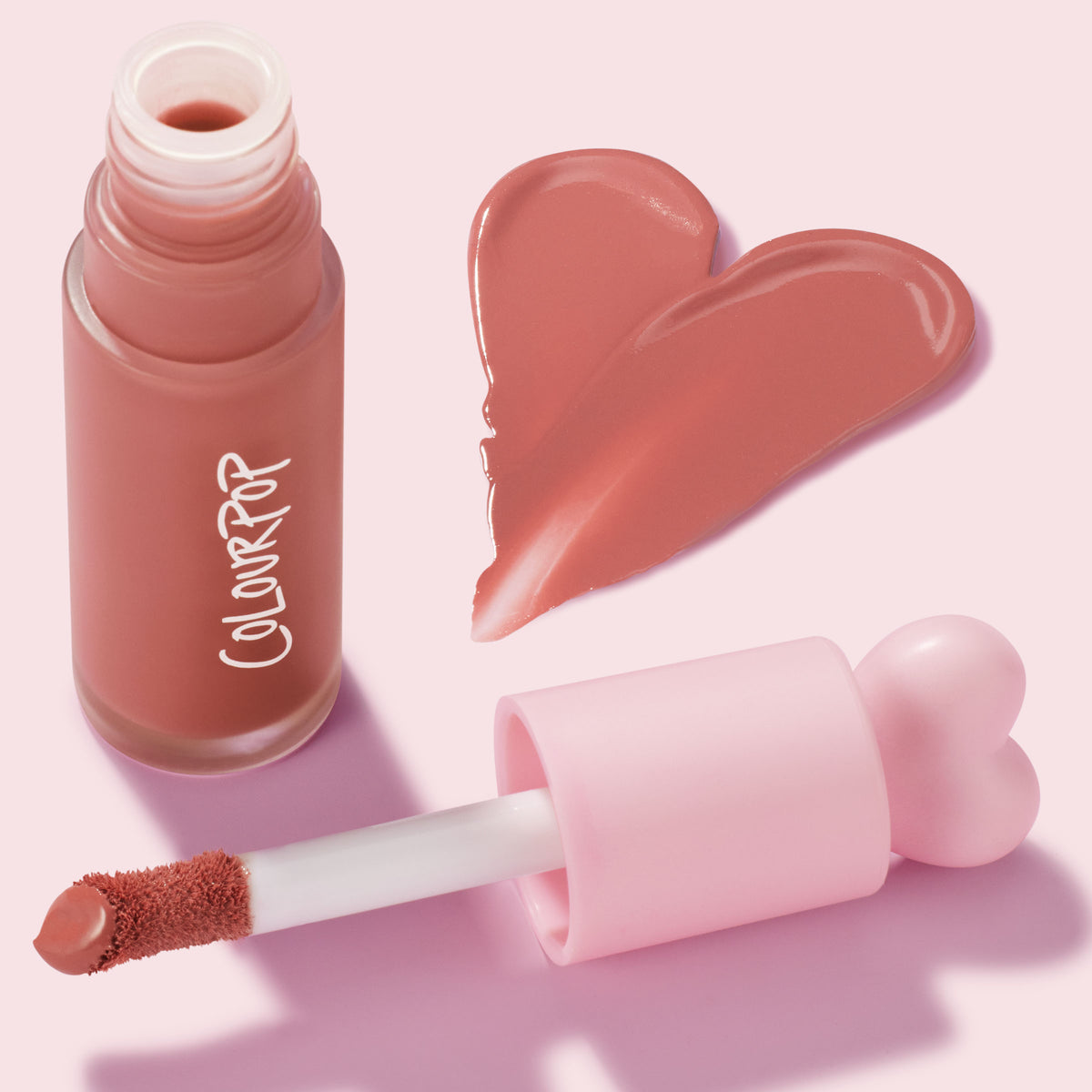 THX shade ColourPop Liquid Blush shown open with doe-foot applicator and heart-shaped pink cap, a glossy rosy-nude heart swatch beside a frosted glass bottle on a pastel pink background.