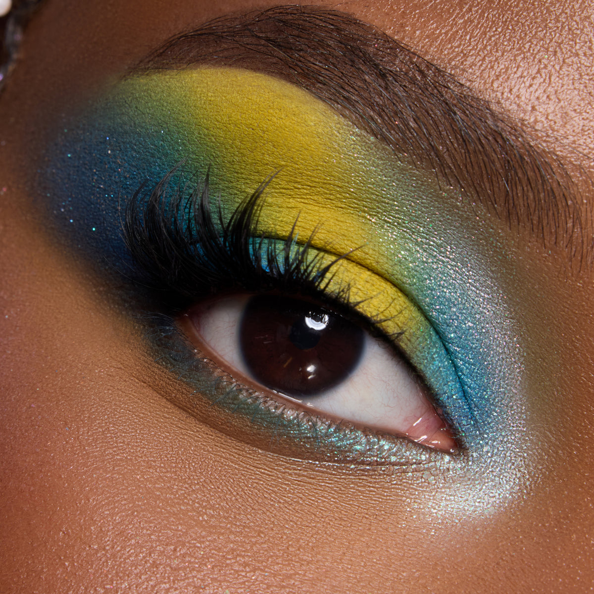 Close-up of a deep-skin eye with bold yellow, teal and blue shadow from the Under the Sea palette