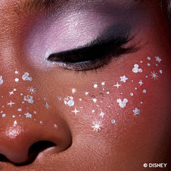 Close-up of glitter freckle tattoos with stars and tiny Mickey Mouse silhouettes across a deep-skin cheek and nose