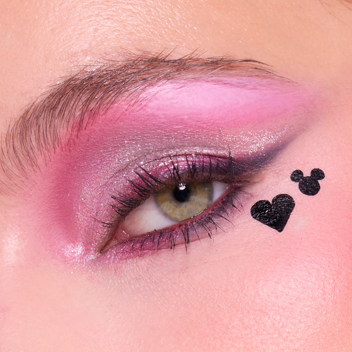 Close-up of a fair-skin eye with pink shadow and a black heart and Mickey Mouse silhouette stamped at the outer corner