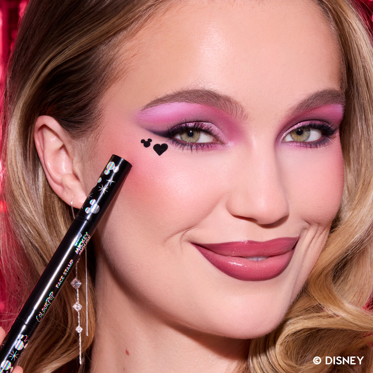 Model with fair skin holding the Merry Mickey Face Stamp, a black Mickey Mouse silhouette and heart stamped by her eye