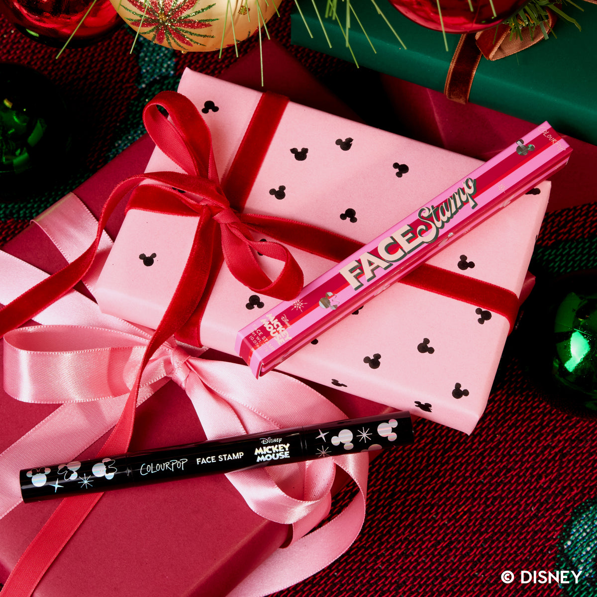 Merry Mickey Face Stamp resting on a pink gift box tied with ribbon among holiday ornaments