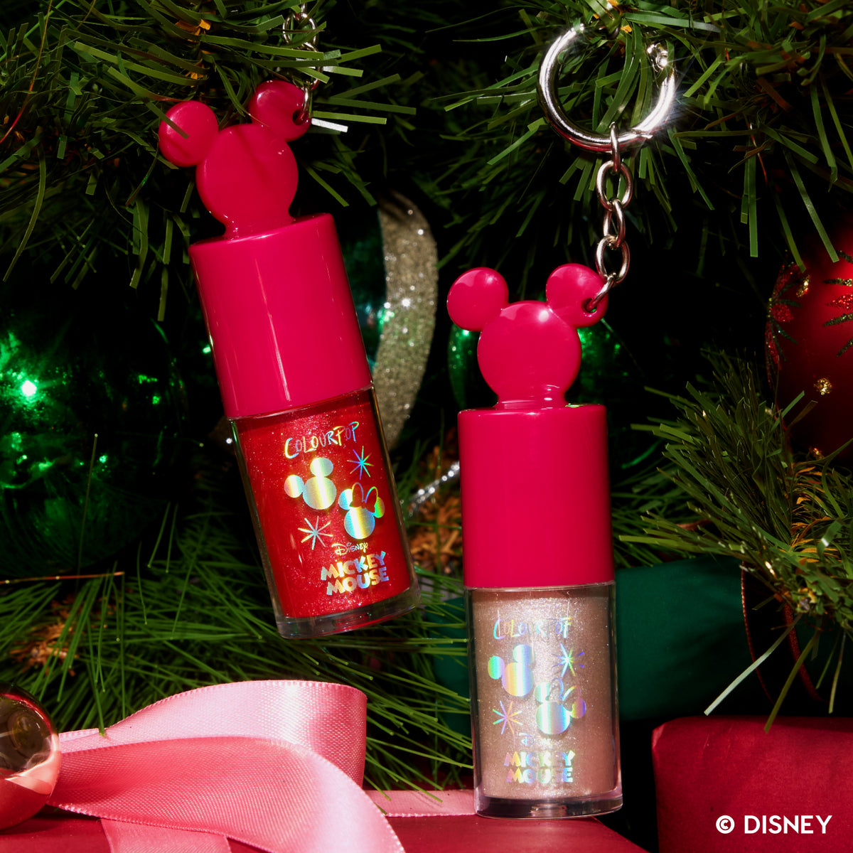 Christmas Kisses and Under the Mistletoe Ultra Glossy Lip keychains hanging on a Christmas tree