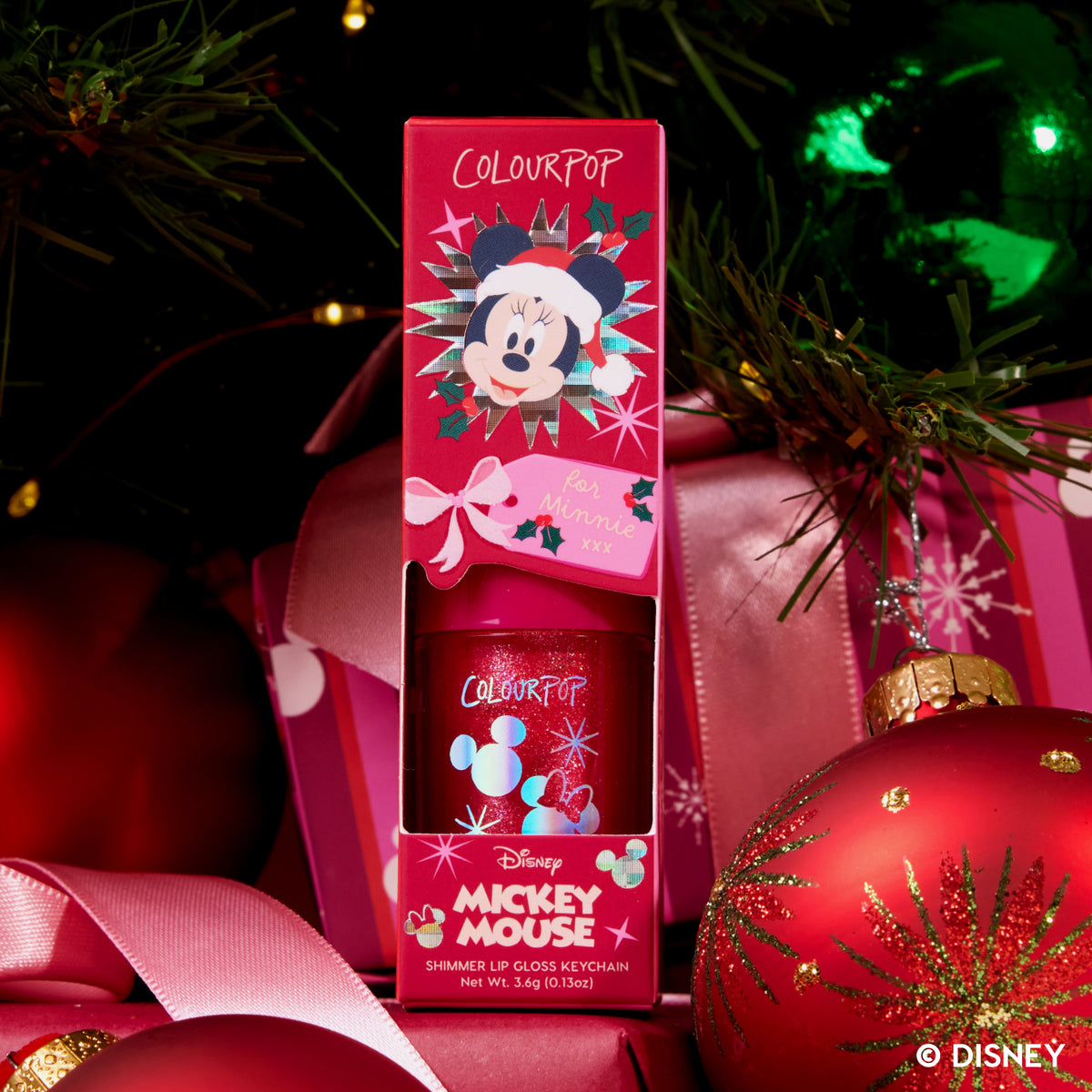 Christmas Kisses Ultra Glossy Lip box among red ornaments under a Christmas tree
