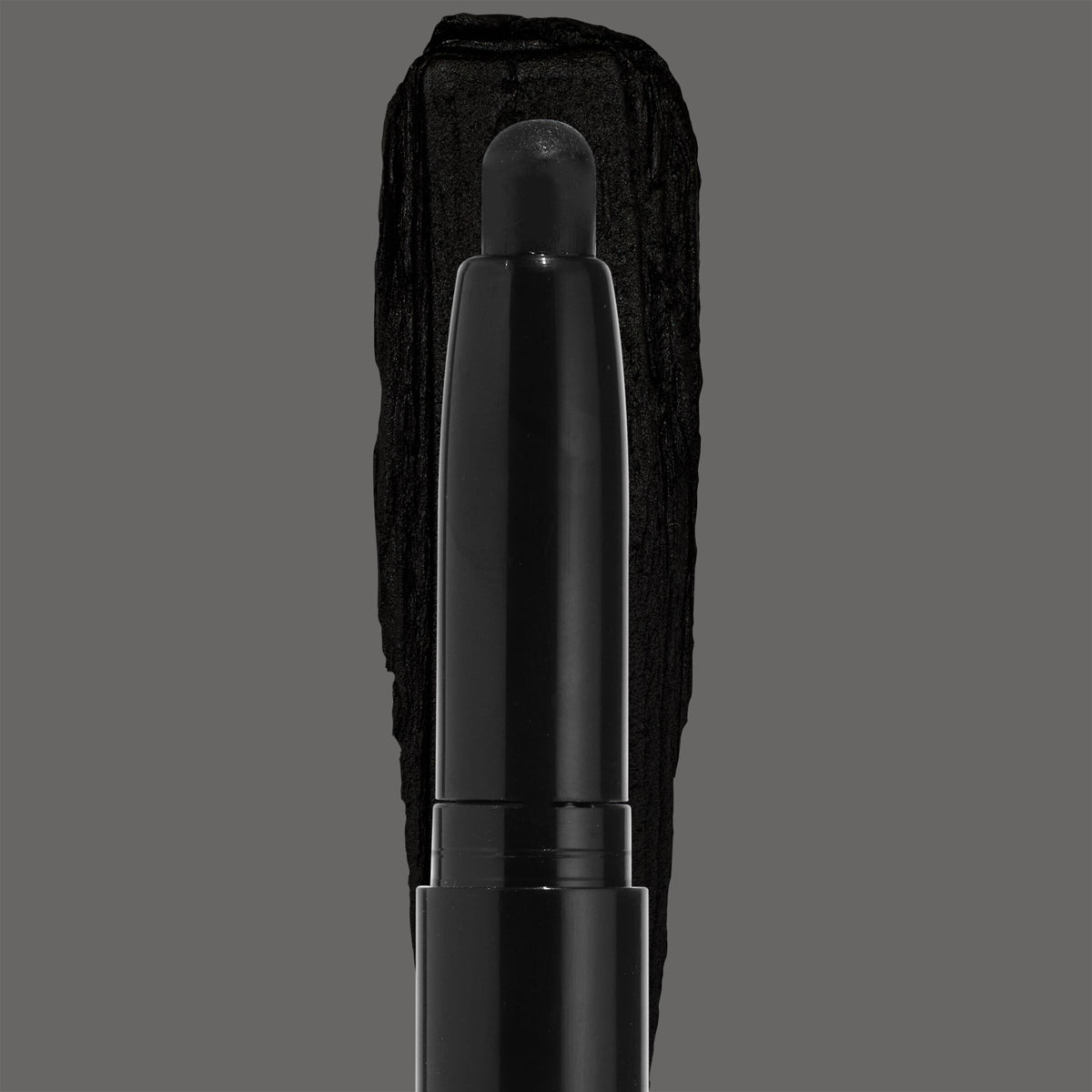 ColourPop Shadow Stix in Midnight Hour depositing a rich jet-black eyeshadow swatch, the rounded stick tip centered over a bold black smear on a gray backdrop, sleek black barrel emphasizing the smoky shade.